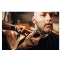 Fotografie Male barber cutting beard of client in barber shop, South_agency, 40 × 26.7 cm