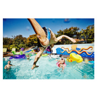 Umělecká fotografie Man in mid air jumping into pool during party, Thomas Barwick, (40 x 26.7 cm