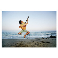 Fotografie Mixed Race man playing guitar and jumping at beach, Peathegee Inc, 40x26.7 cm