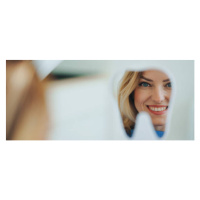 Fotografie Happy patient looking at her teeth in mirror., Halfpoint Images, 50 × 21.4 cm