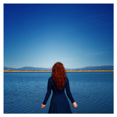 Fotografie Redhead in blue dress faces rippled lake, Anna Gorin, 40 × 40 cm